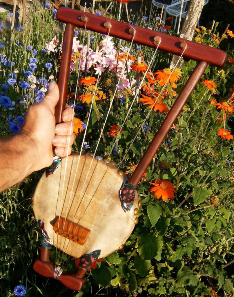 A person playing a wooden harp in a flower garden.