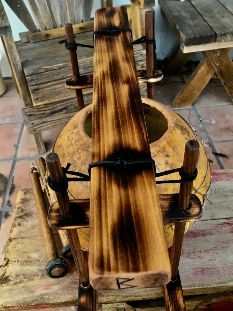 A wooden loom is sitting on top of a wooden table, alongside gourd instruments.