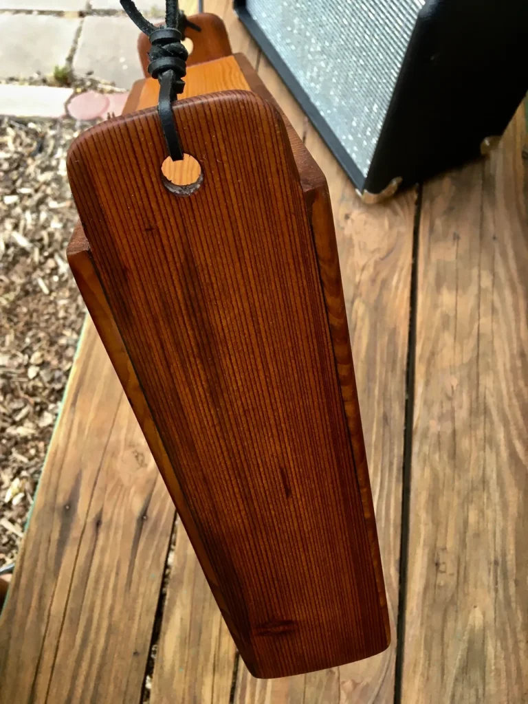 A wooden guitar strap hanging on a wooden deck, alongside a gourd instrument.