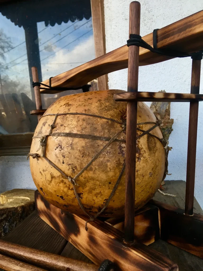 A large wooden ball, resembling a gourd instrument, sitting on a wooden stand.