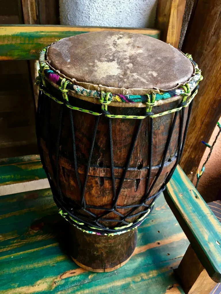 A wooden djembe, made of Ilimba wood, sitting on a wooden bench.