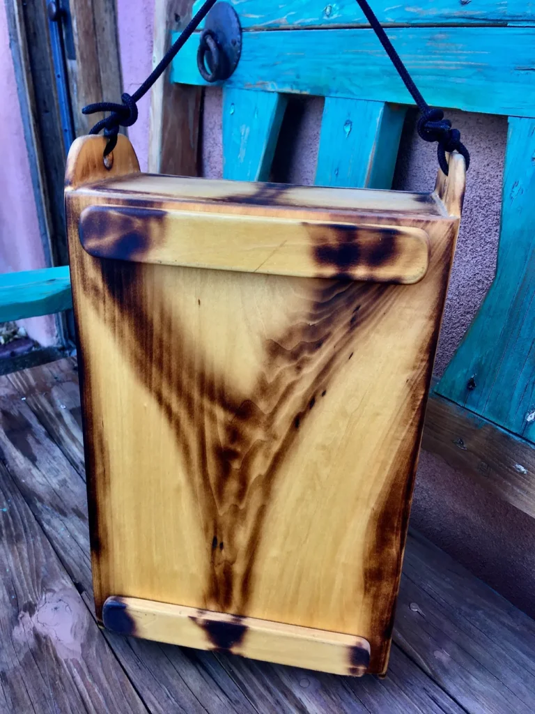 A wooden box, resembling a Kalimba, sitting on a wooden bench.