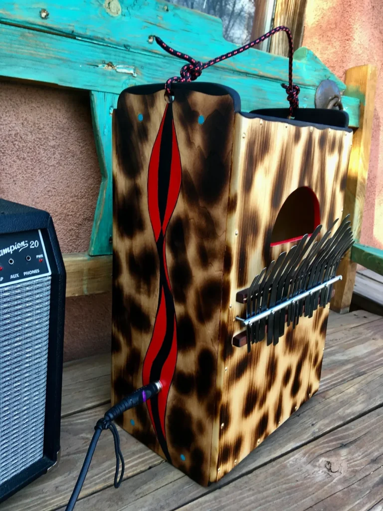 A wooden box with a leopard print on it sits on a wooden deck, alongside an African drum.