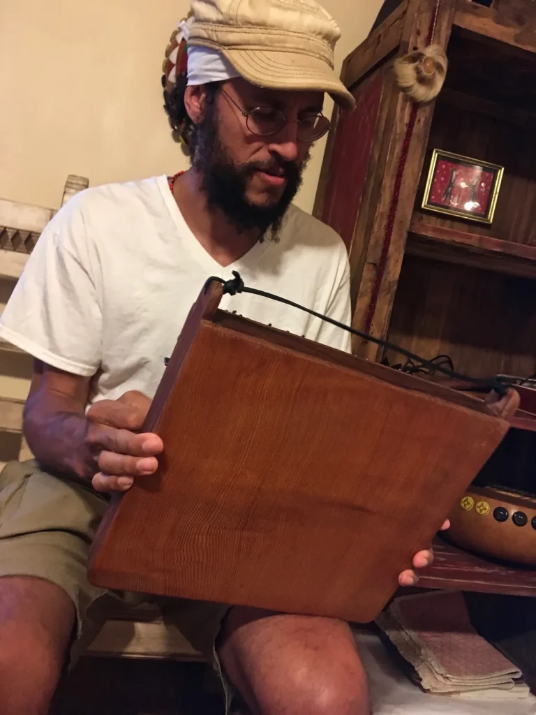 A man in a hat is holding a wooden box containing gourd instruments.