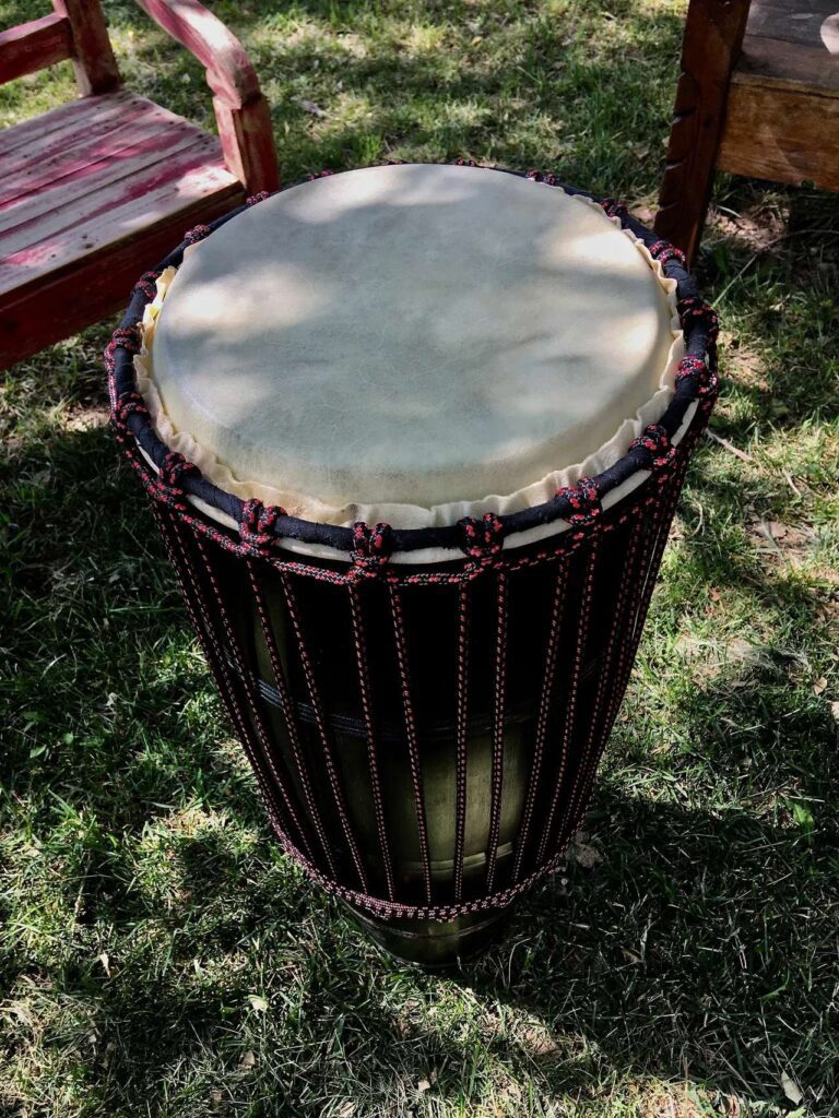 A djembe drum sitting on the grass next to a chair, accompanied by an ilimba.