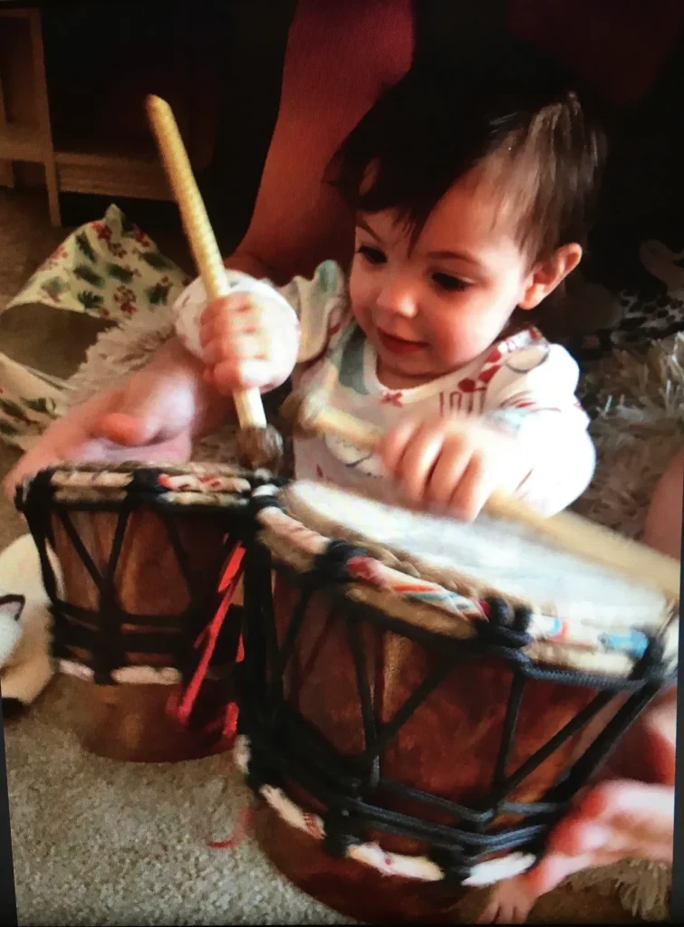 A baby is playing drums on the floor while occasionally experimenting with African harps.