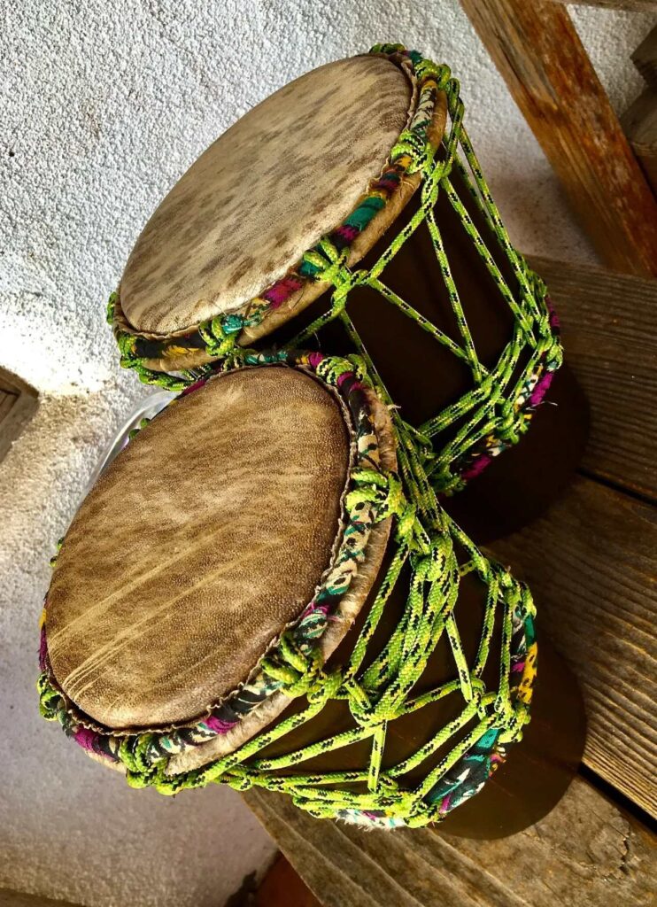 Two wooden djembes, traditional African drums, sitting on a wooden bench.