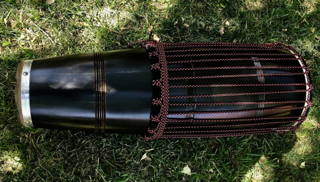 A black drum, made of Ilimba wood, sitting on the grass.