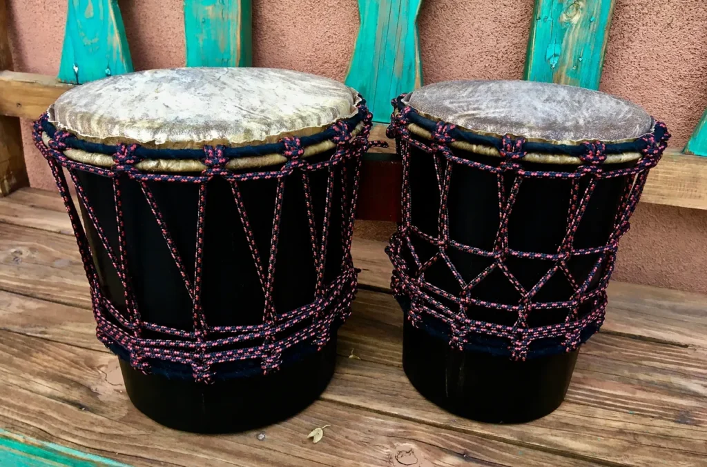 Two djembe drums, traditional African percussion instruments, sitting on a wooden bench.