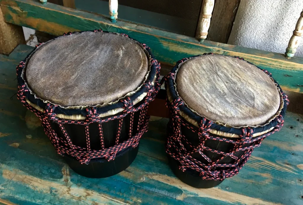 Two wooden djembes, traditional African drums, sitting on a wooden bench.