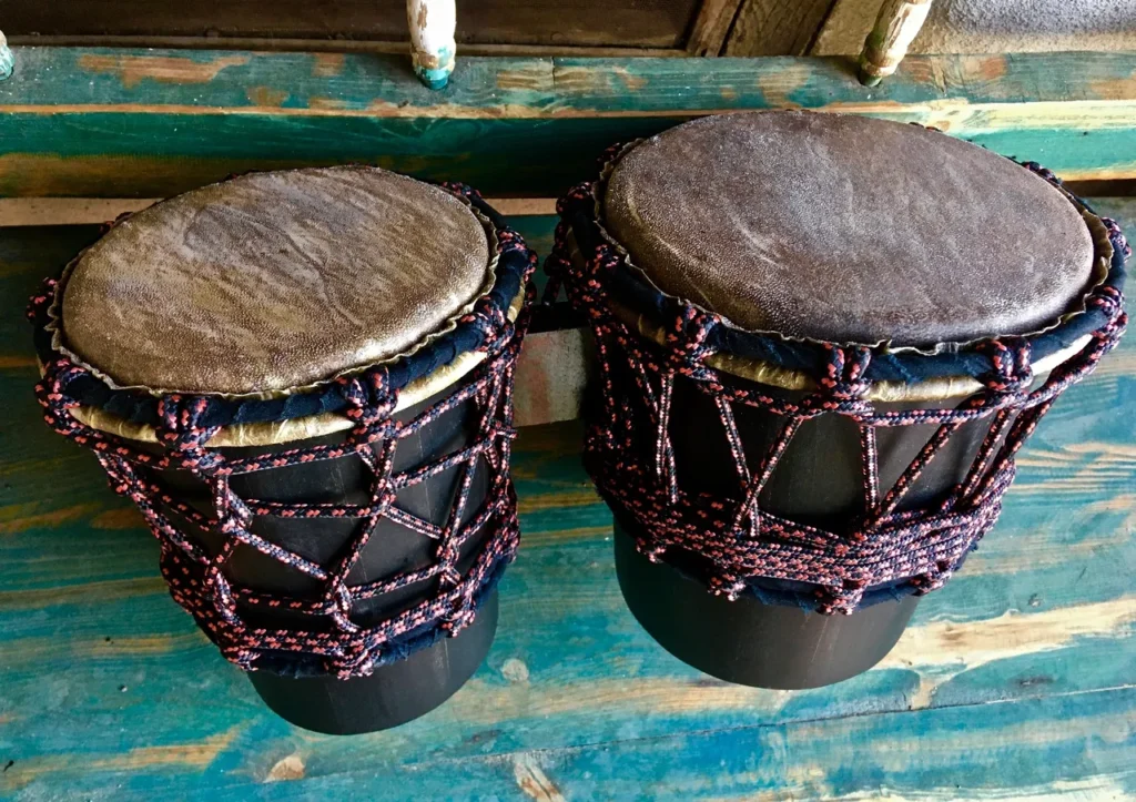 Two djembe drums hanging on a wooden wall, representing African percussion.