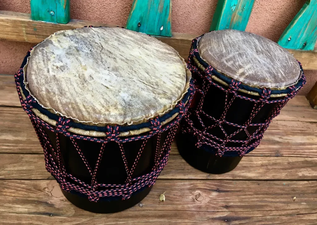 Two djembe drums, traditional African percussion instruments, sitting on a wooden bench.