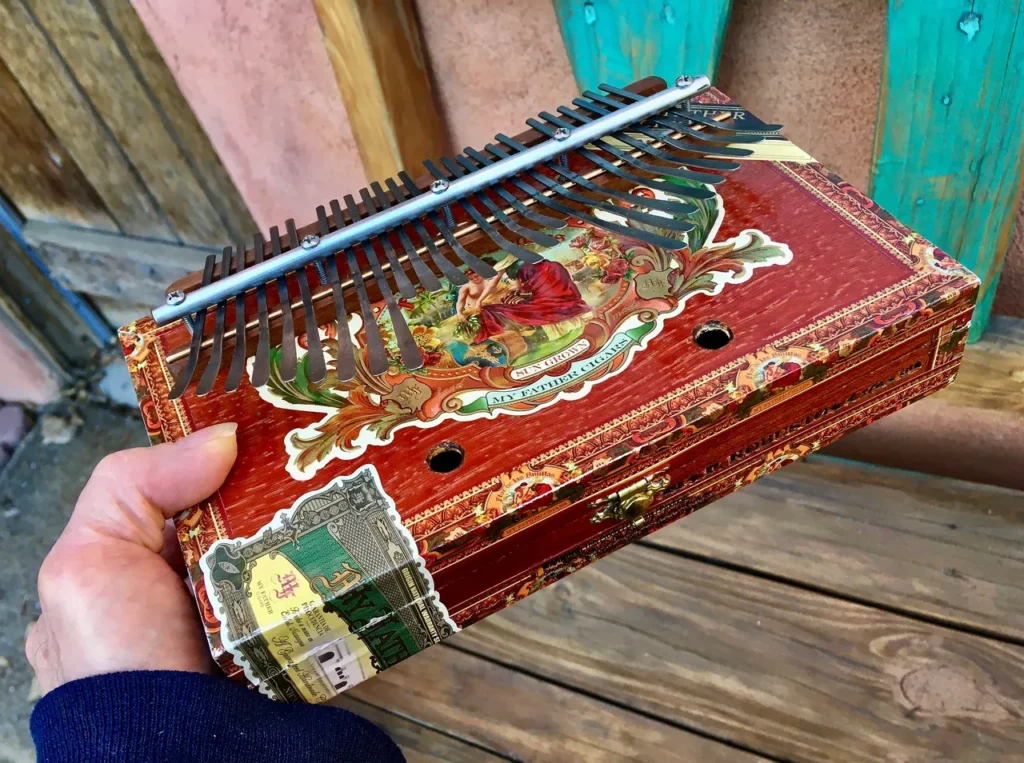 A person holding an Ngoma, a wooden accordion used in African music, inside a wooden box.