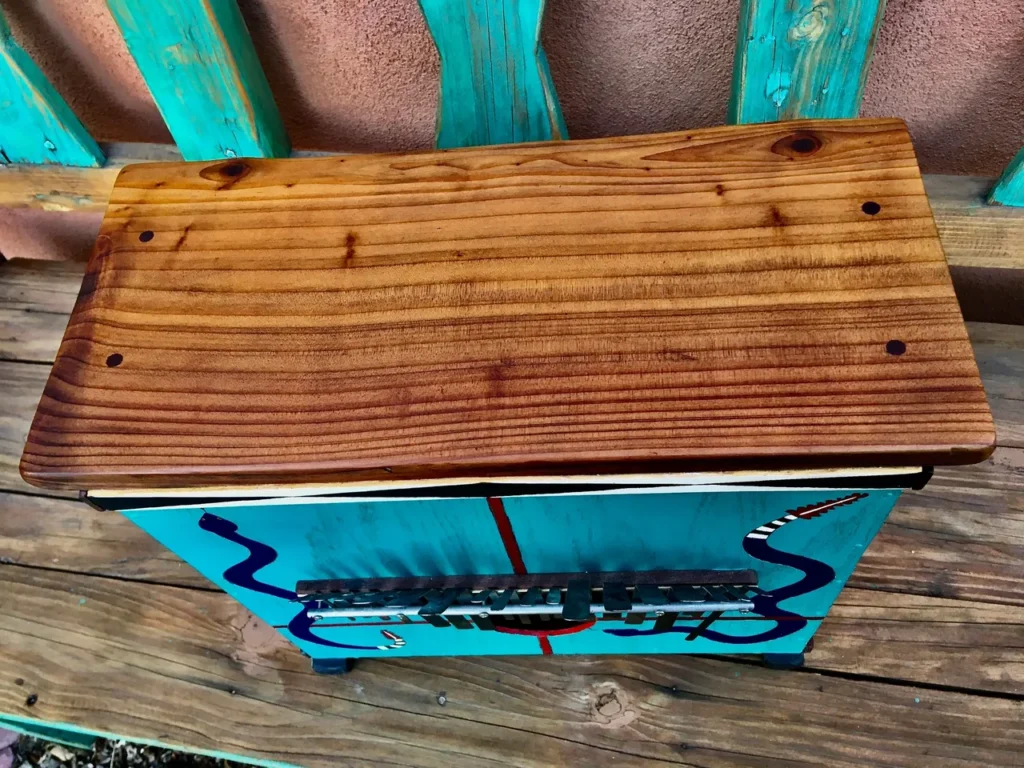 A wooden box featuring a Kalimba sitting on a wooden bench.