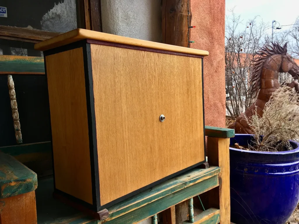 A wooden cabinet sitting on a wooden bench, accompanied by an African drum.