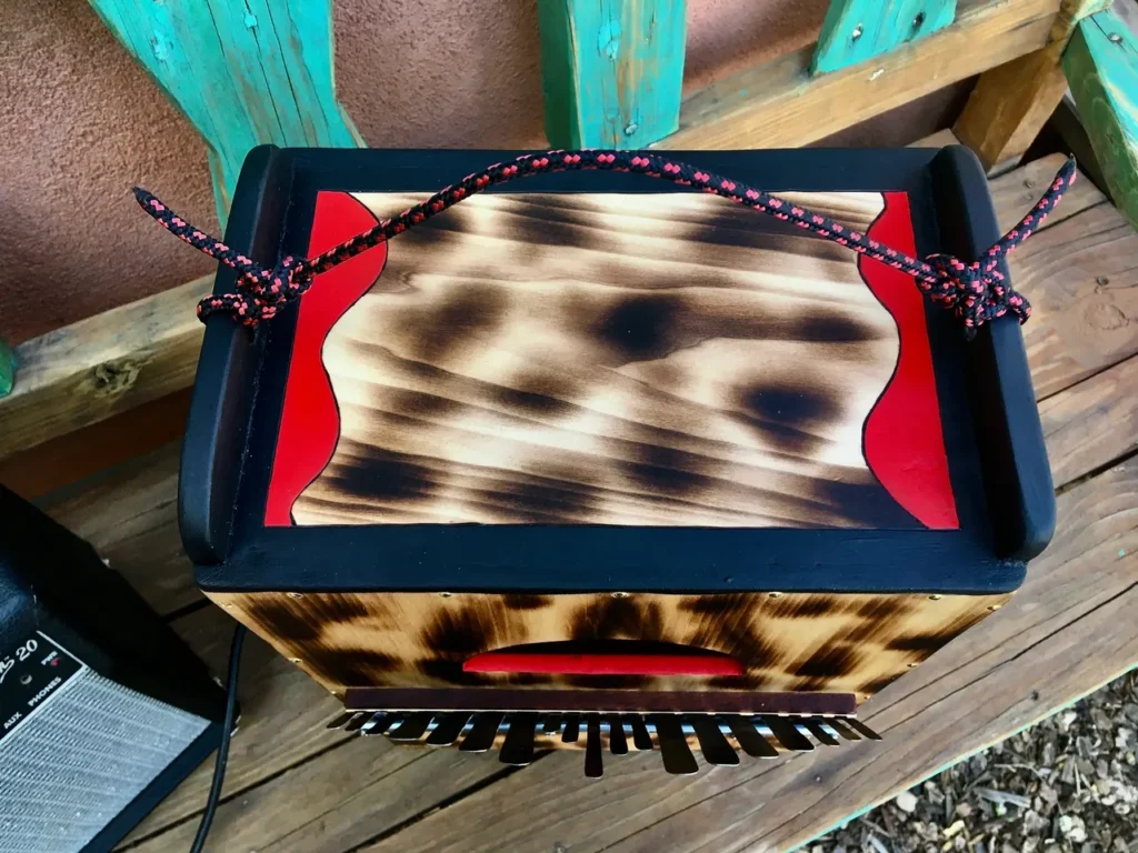 A wooden accordion and an African drum sitting on a wooden deck.