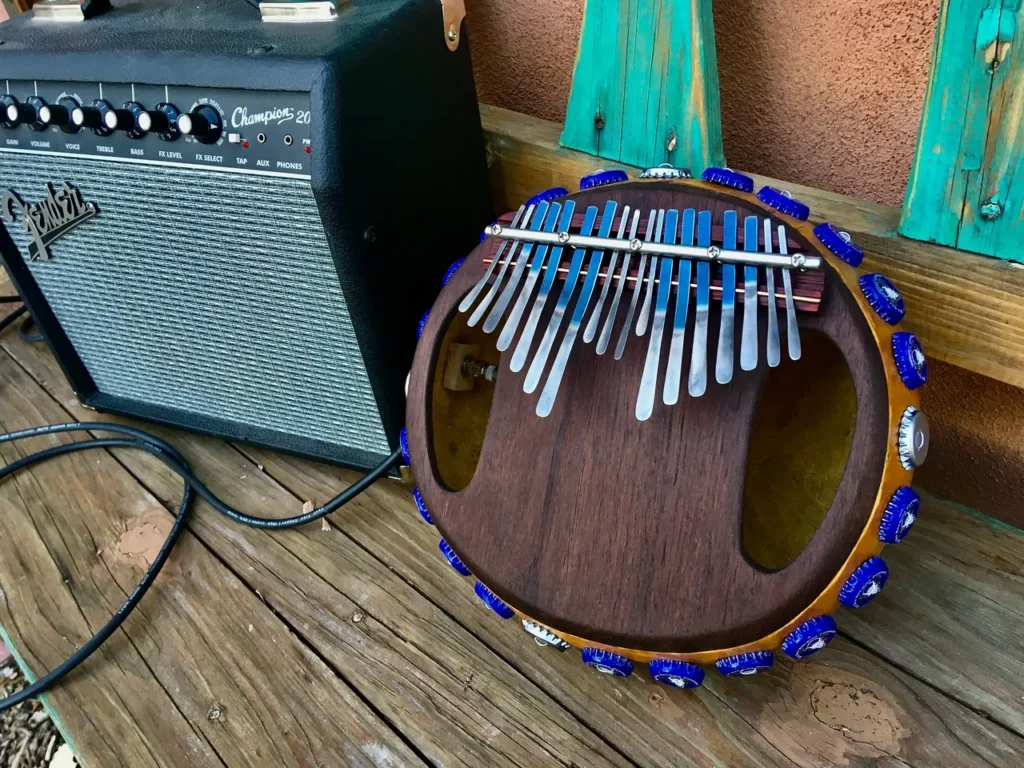 An acoustic guitar sits on a wooden bench, accompanied by an Ilimba.