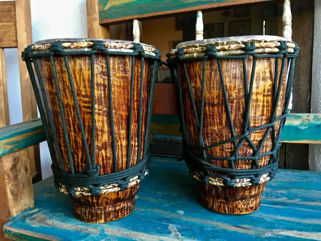 Two wooden djembes sitting on a wooden bench.