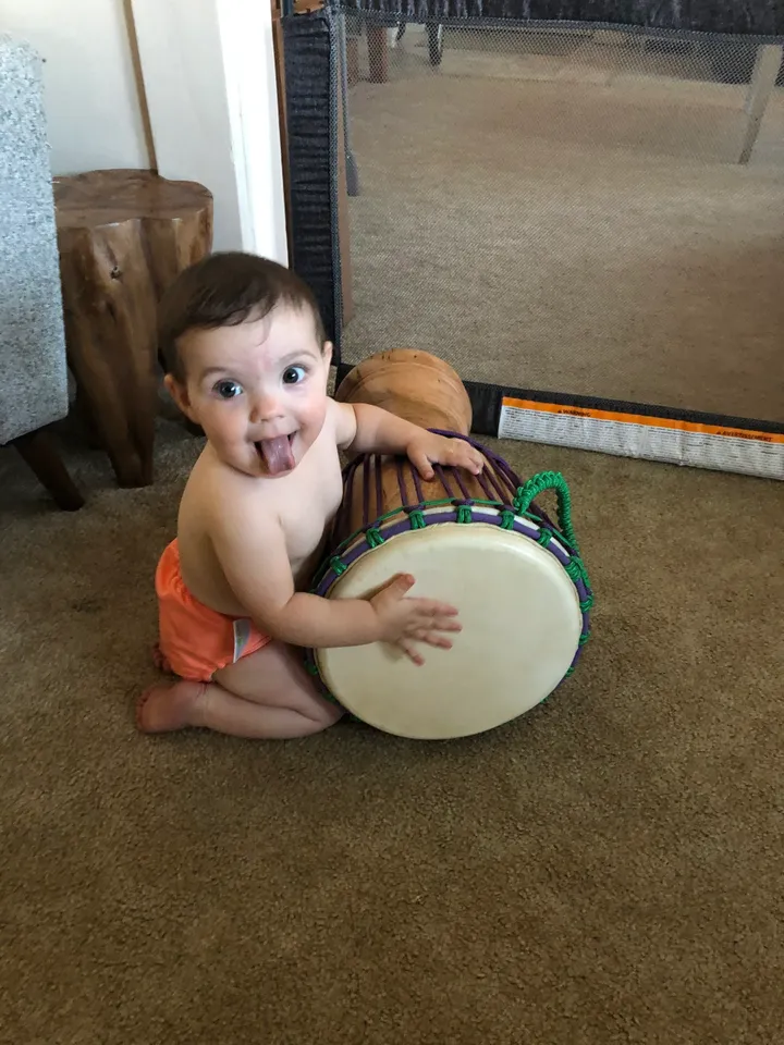 A baby sitting on the floor with a kongoma drum.