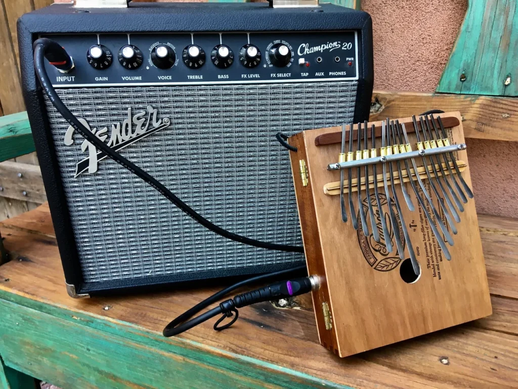 A wooden kalimba, also known as a lamellaphone, rests on a wooden bench alongside a classic guitar amplifier.