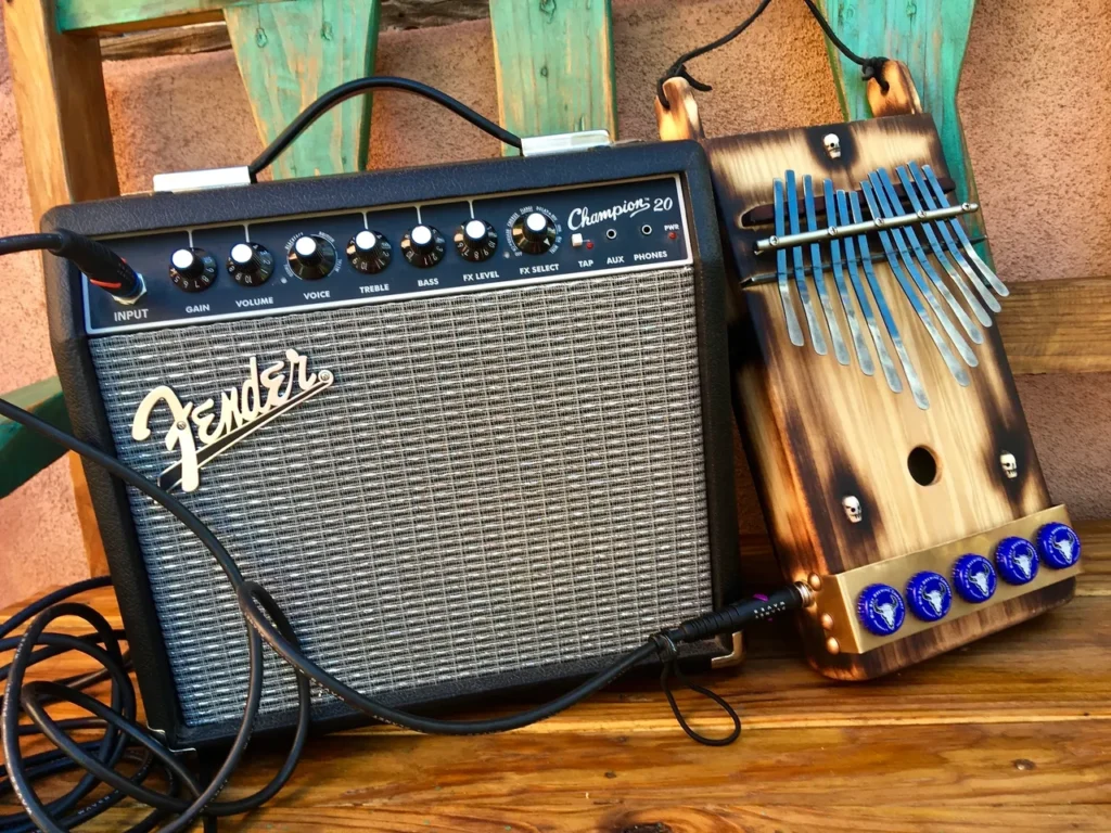 A guitar amplifier and a ukulele, both resting on a wooden bench.