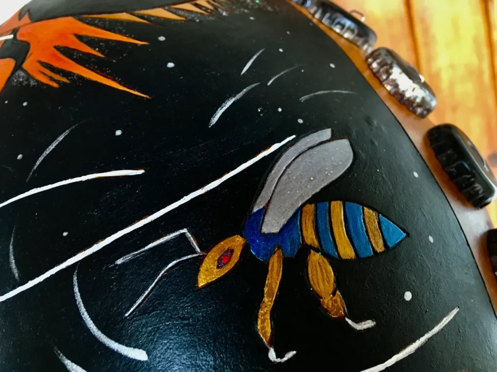         Description: A black vase with a bee painted on it, inspired by African harps.