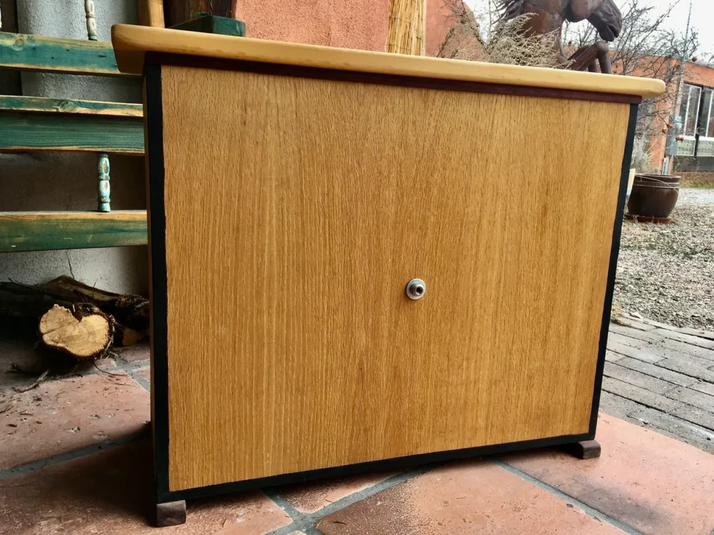 A small wooden cabinet with a Kalimba sitting on a tiled floor.