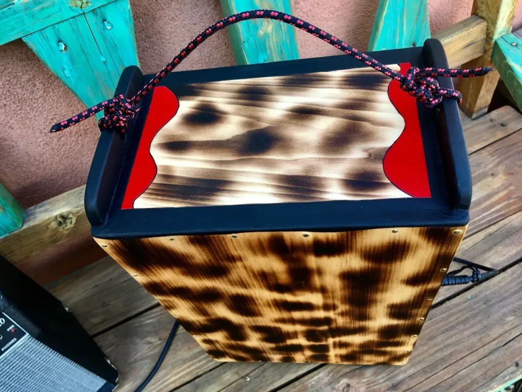 A wooden box is sitting on a wooden deck, next to a Kalimba.