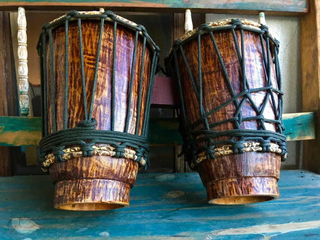 Two wooden djembes, traditional African drums, sitting on a wooden bench.