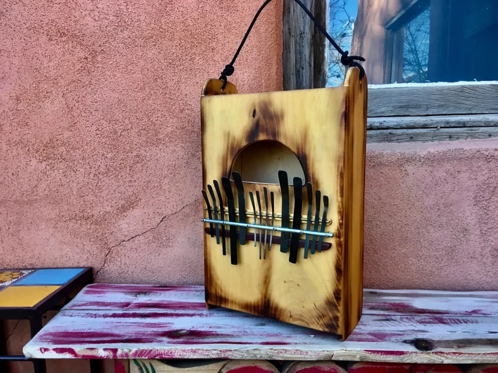 A wooden box, resembling a Kalimba, sitting on a bench next to a wall.