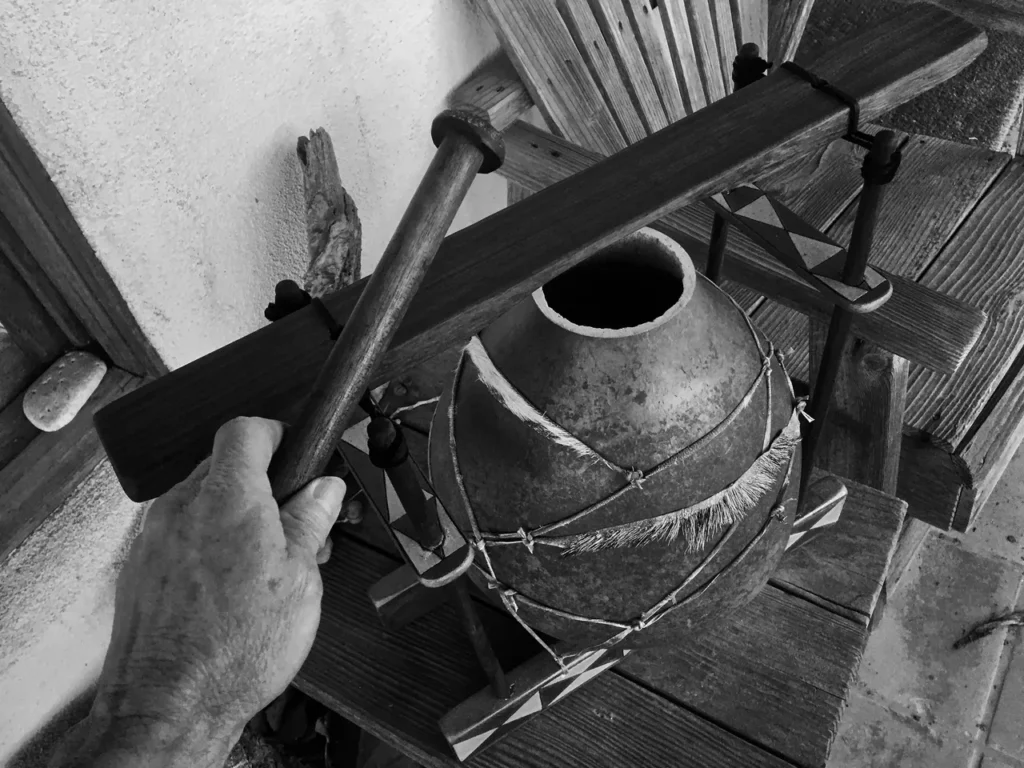 A hand is holding a gourd lamellaphone on a wooden table.