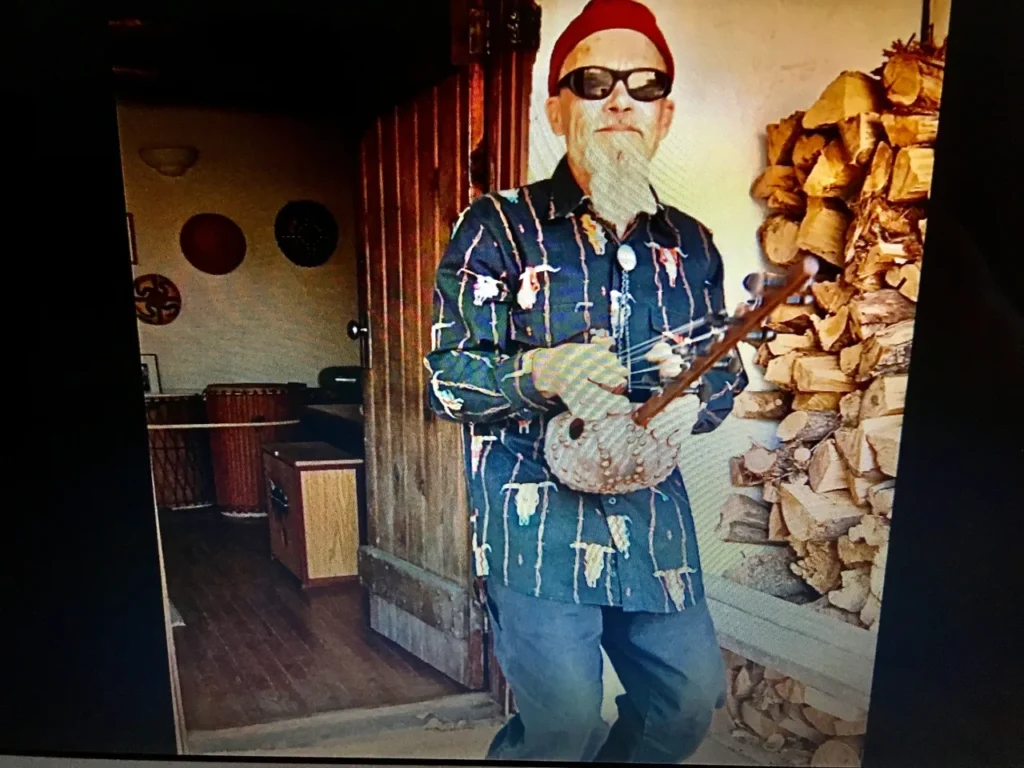 An African man with a beard and sunglasses is holding a Ngoma, a traditional African musical instrument.