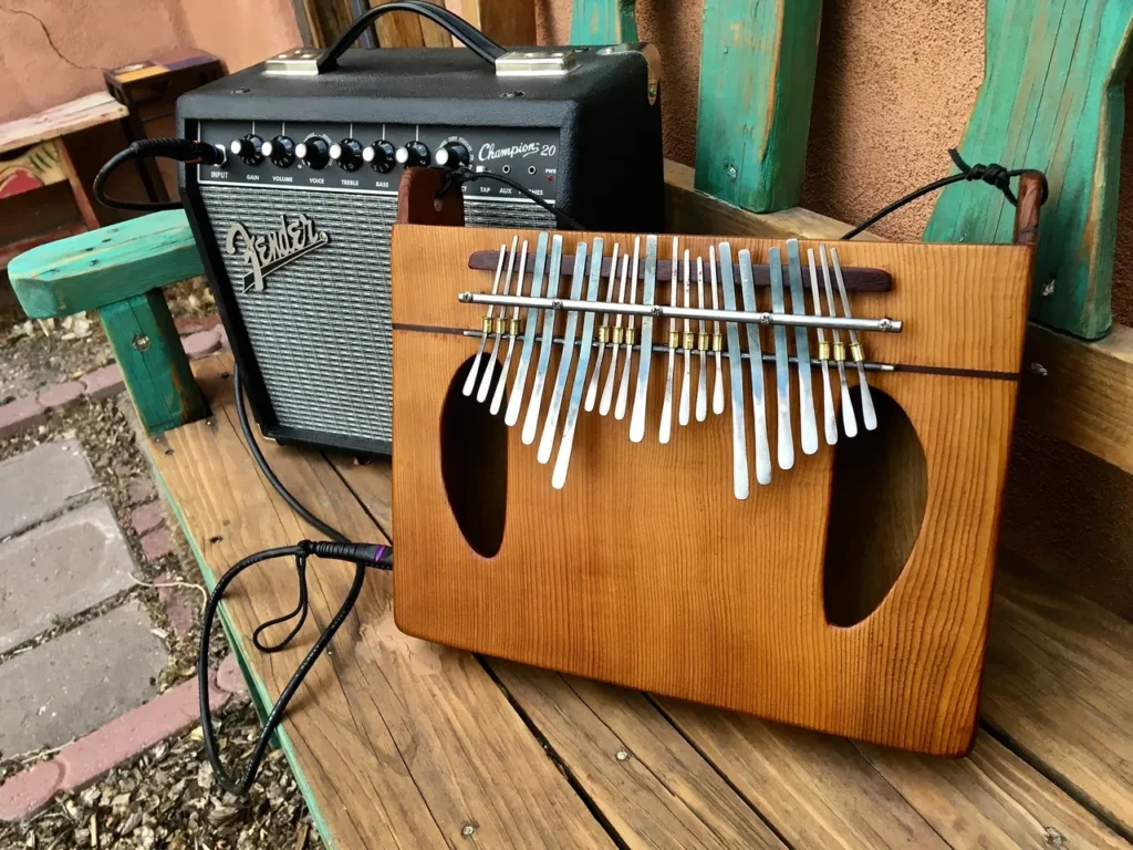 A gourd instrument, resembling a lamellaphone, is sitting on a wooden bench next to a guitar.