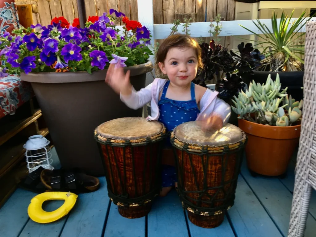 A little girl playing a djembe, an African drum, on a deck.