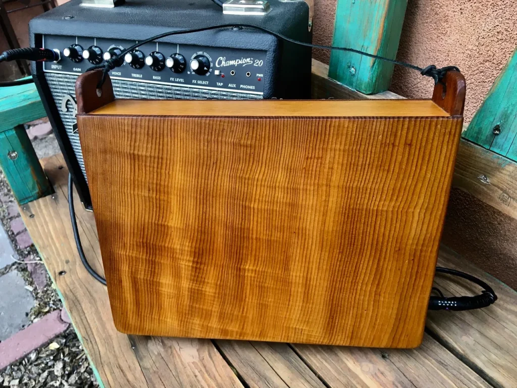 A wooden guitar amplifier sitting on a wooden bench.