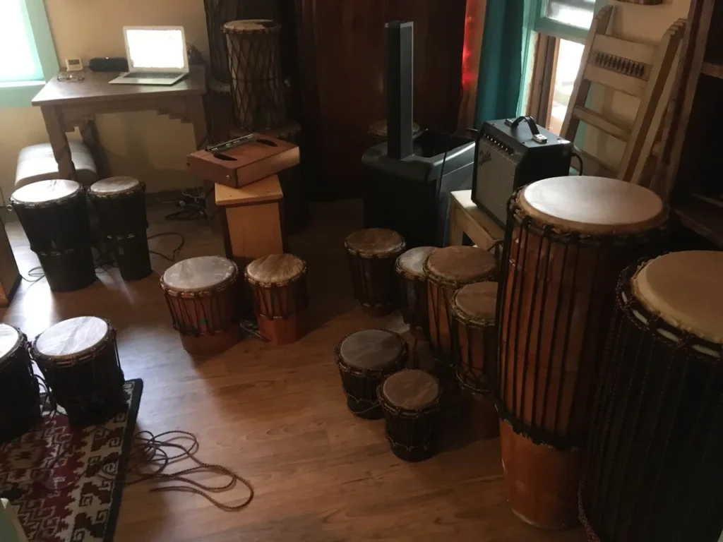 Djembes and drums, accompanied by African harps, fill the room alongside a laptop.