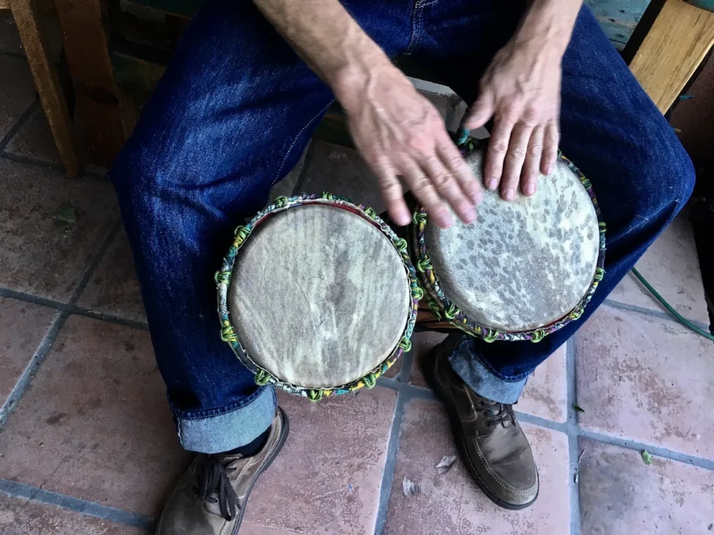 A man playing an African harp, also known as the Ilimba, on a wooden bench.