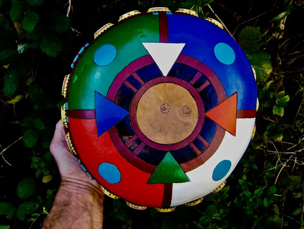 A person holding a Ngoma drum in front of bushes.