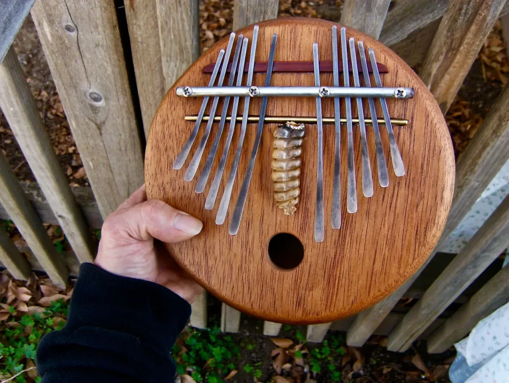 A person holding a wooden ukulele in front of a Ngoma.