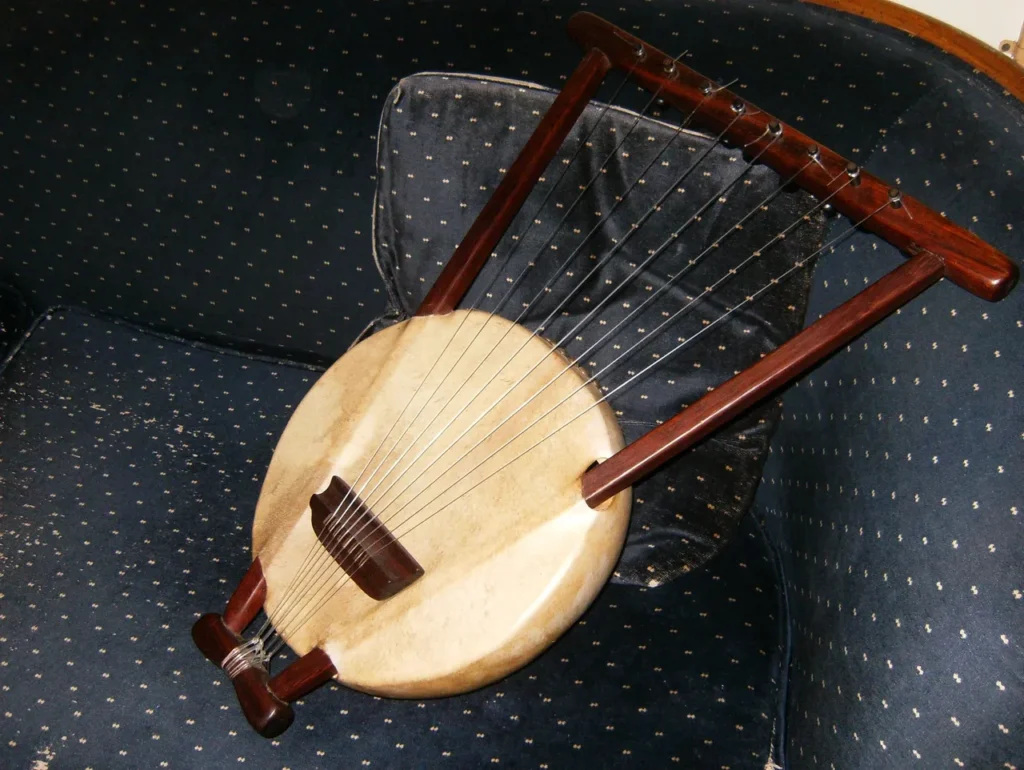 A wooden harp sitting on a blue chair alongside an African drum.