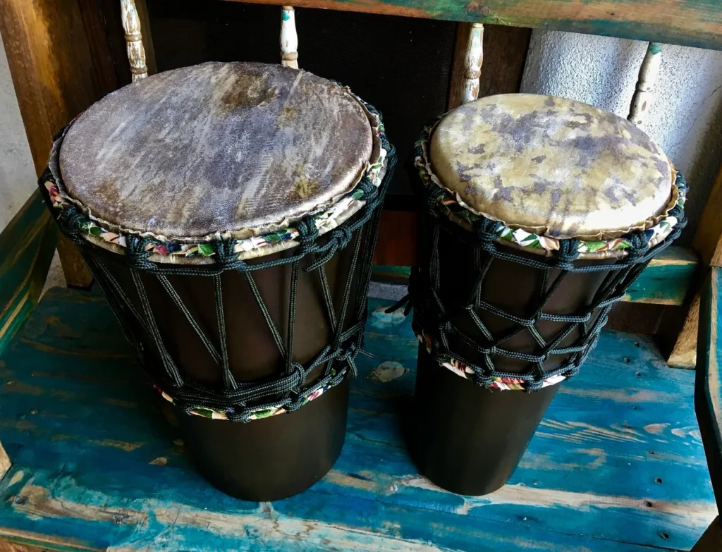 Two djembe drums sitting on a wooden bench, reminiscent of African percussion.