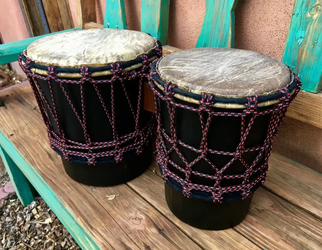 Two djembe drums, an African harps, sitting on a wooden bench.