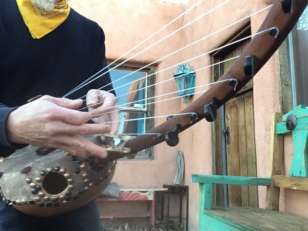 A Ngoma musician is holding a wooden harp, called a ngoma, in front of an African house.