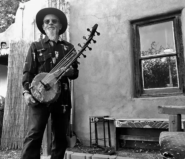 An Ngoma musician with a guitar in front of a house.