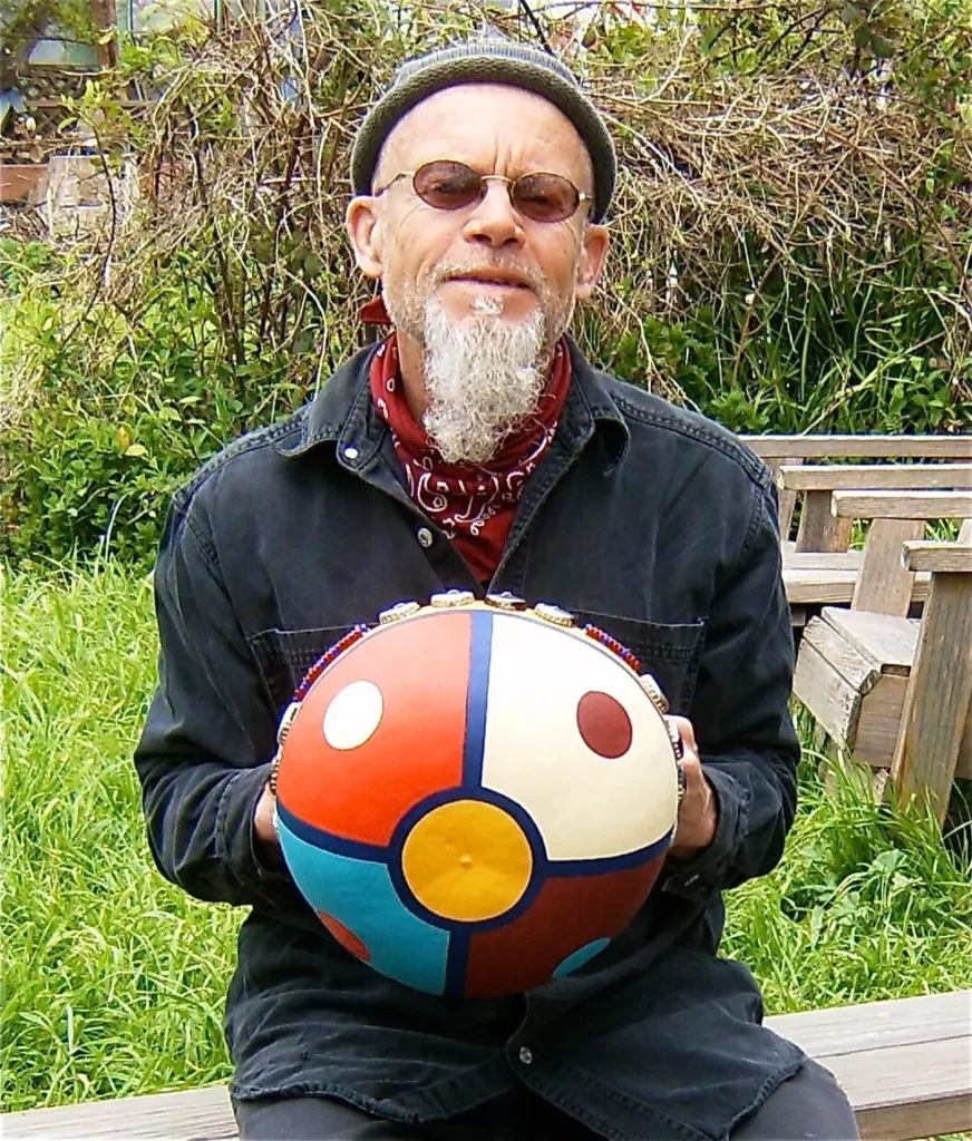 A man sitting on a bench with an Ilimba, a colorful ball in his hand.