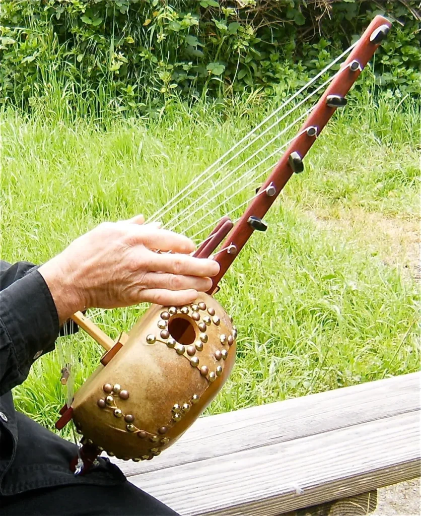 An African man playing a Ngoma, a traditional wooden instrument, on a bench.