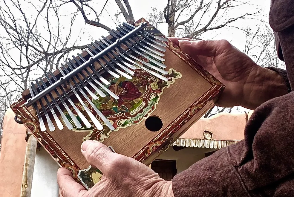 A Ngoma musician showcasing the traditional African music with a wooden accordion in front of a house.