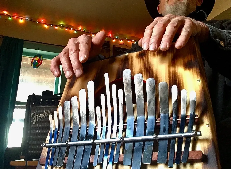 A man in a hat is holding a wooden instrument known as Kalimba.