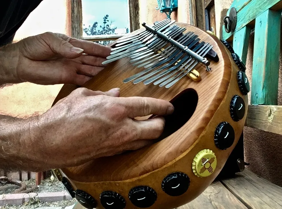 A man is playing an African harp, also known as Ilimba, on a wooden bench.