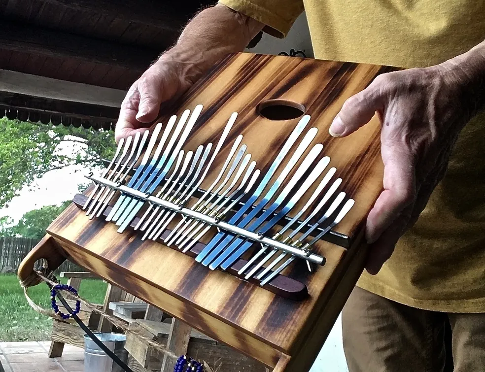 A man is holding a Ngoma, a wooden instrument used in African music, with a lot of different utensils.